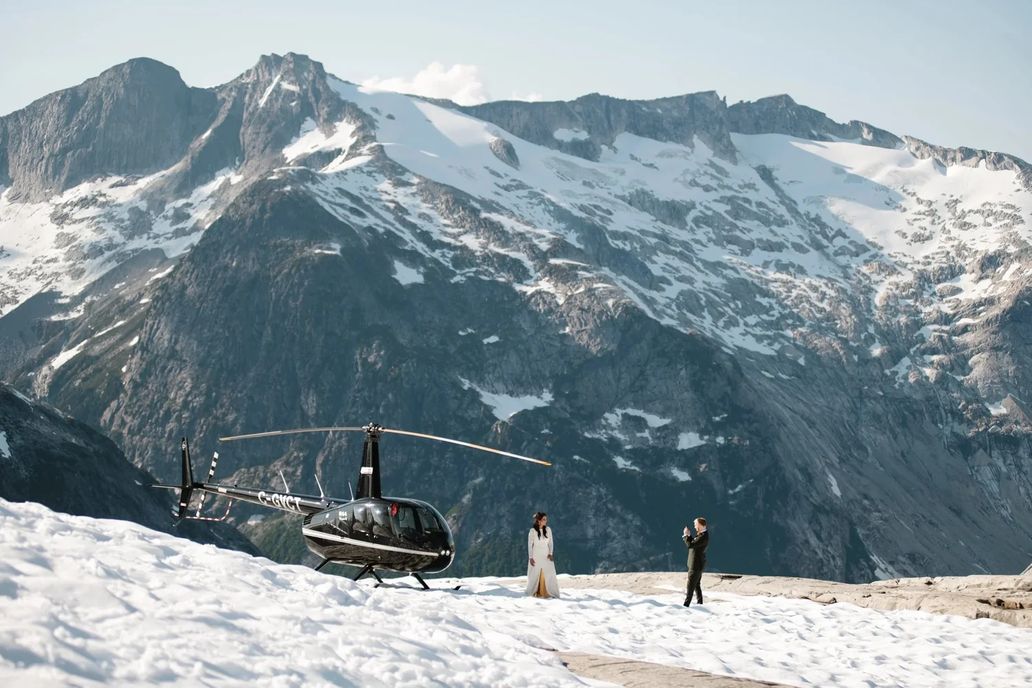 A couple and their helicopter on a snowy mountaintop