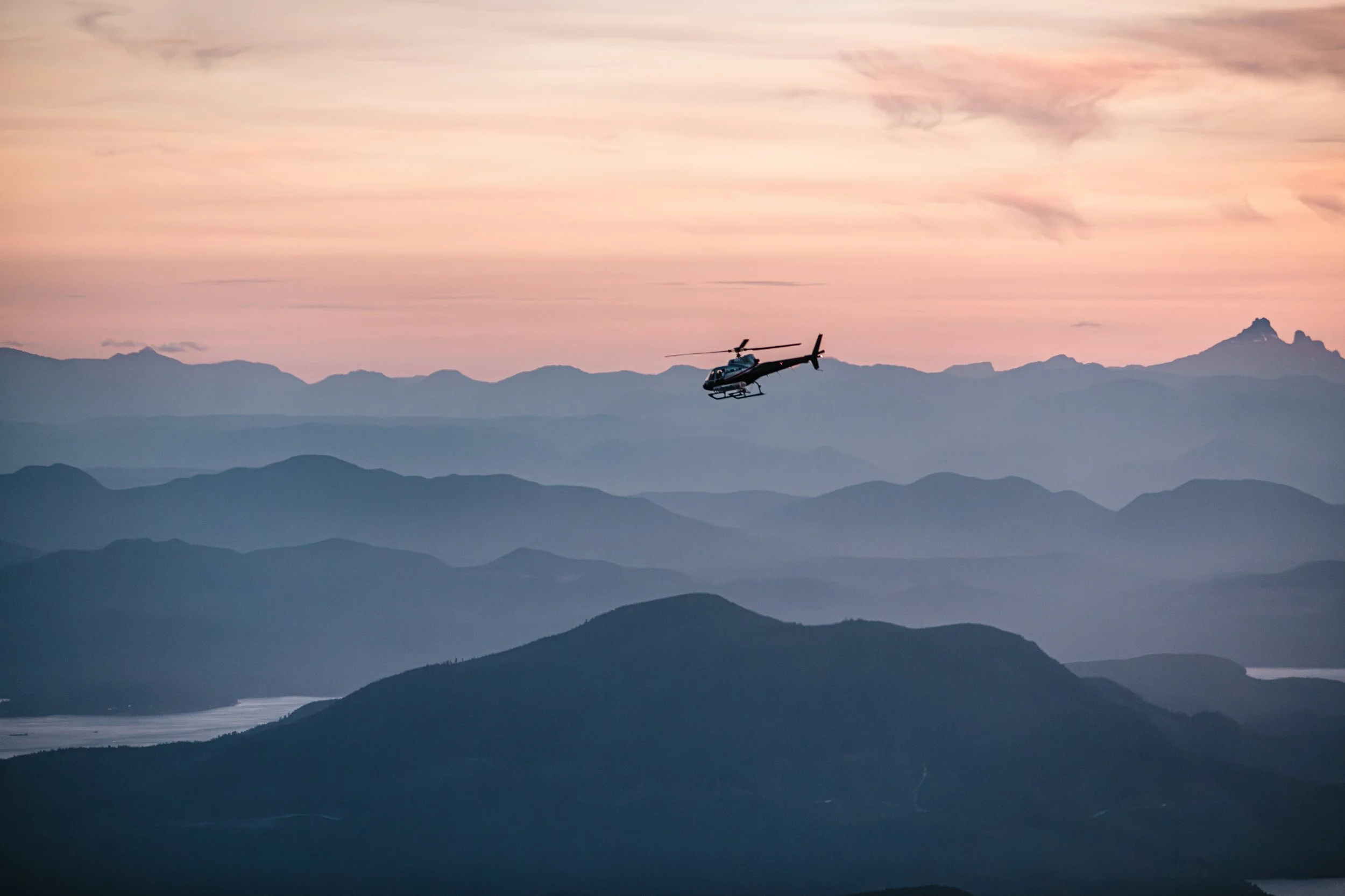 A helicopter flying over layered mountain ridges at dusk