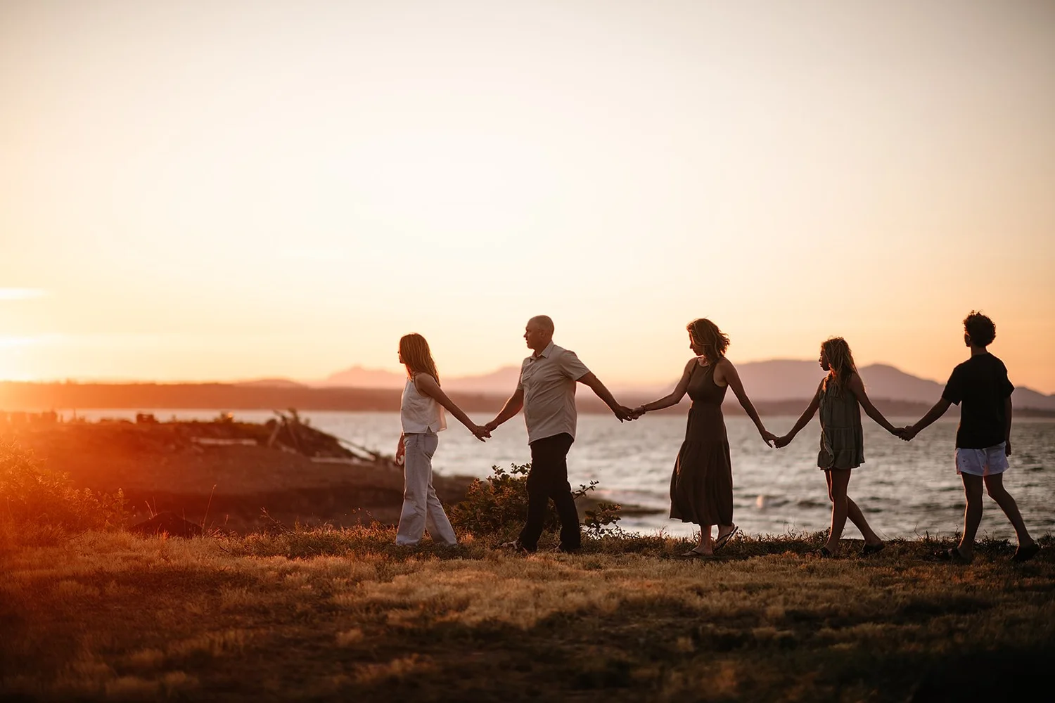 A family holding hands in a line along the shore at sunset