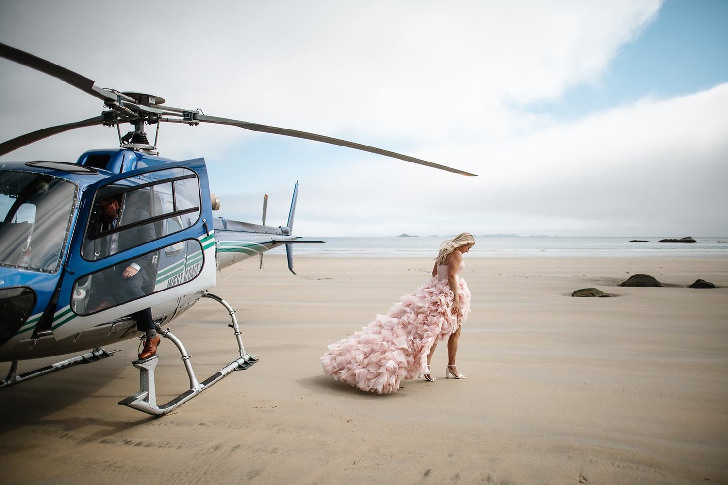 Kelsey in her blush gown beside a helicopter on a wide beach, Nimmo Bay