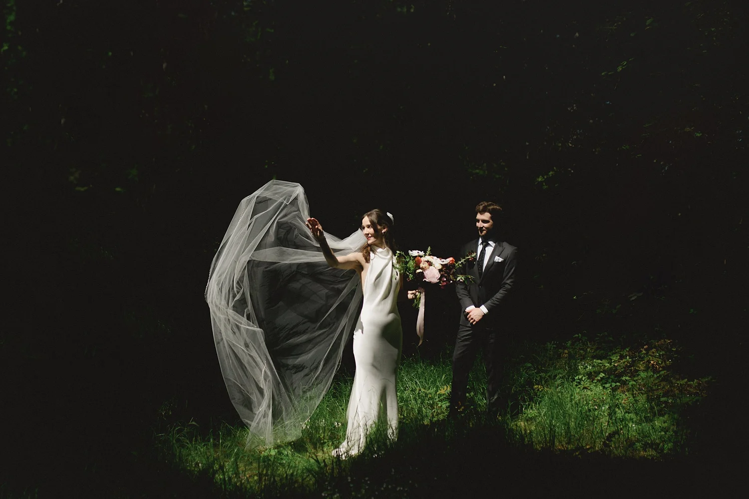 Dana and Cole standing together in the forest as light falls on her veil, Miracle Beach