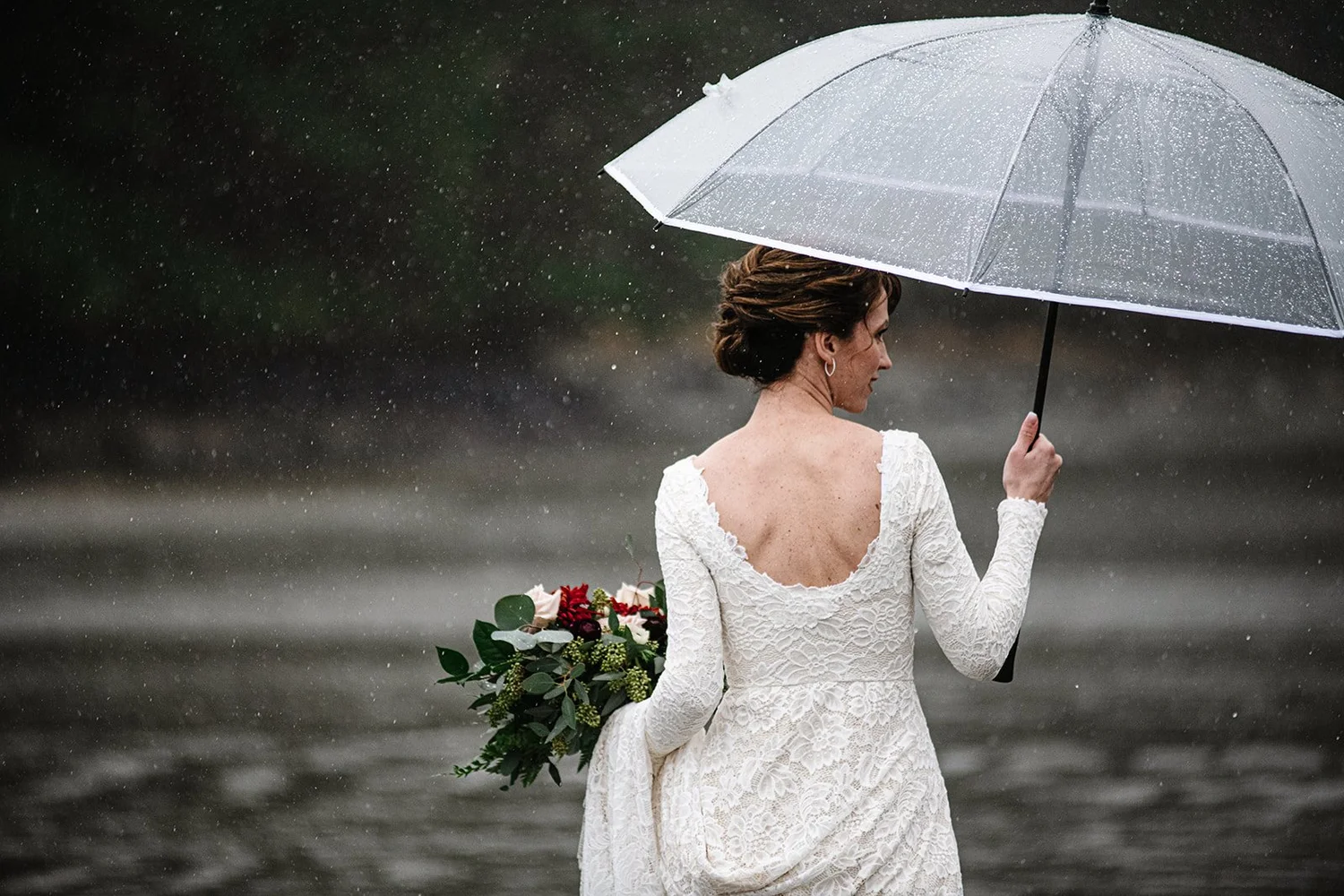 A bride holding a clear umbrella and bouquet in the rain