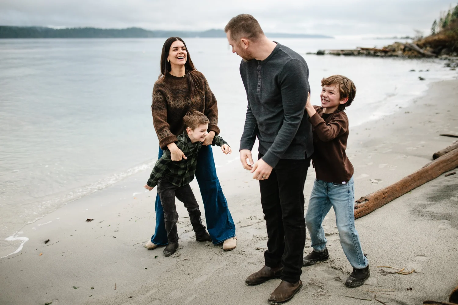 A family of four laughing together on a pebble beach
