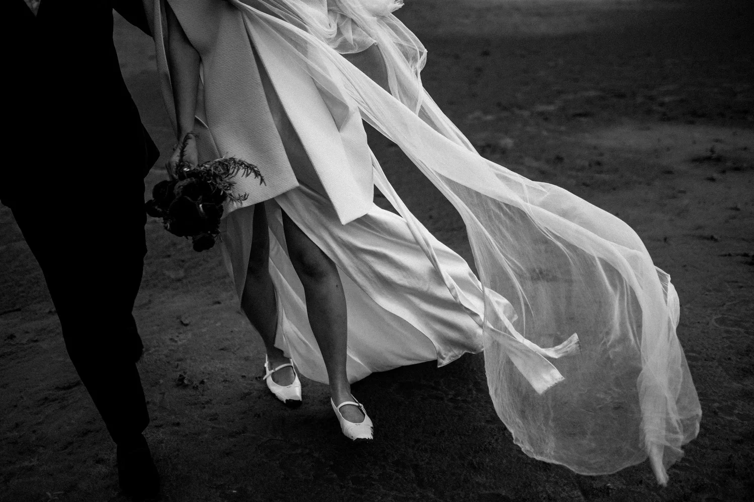 A bride walking hand in hand with her groom as her dress and veil catch the wind