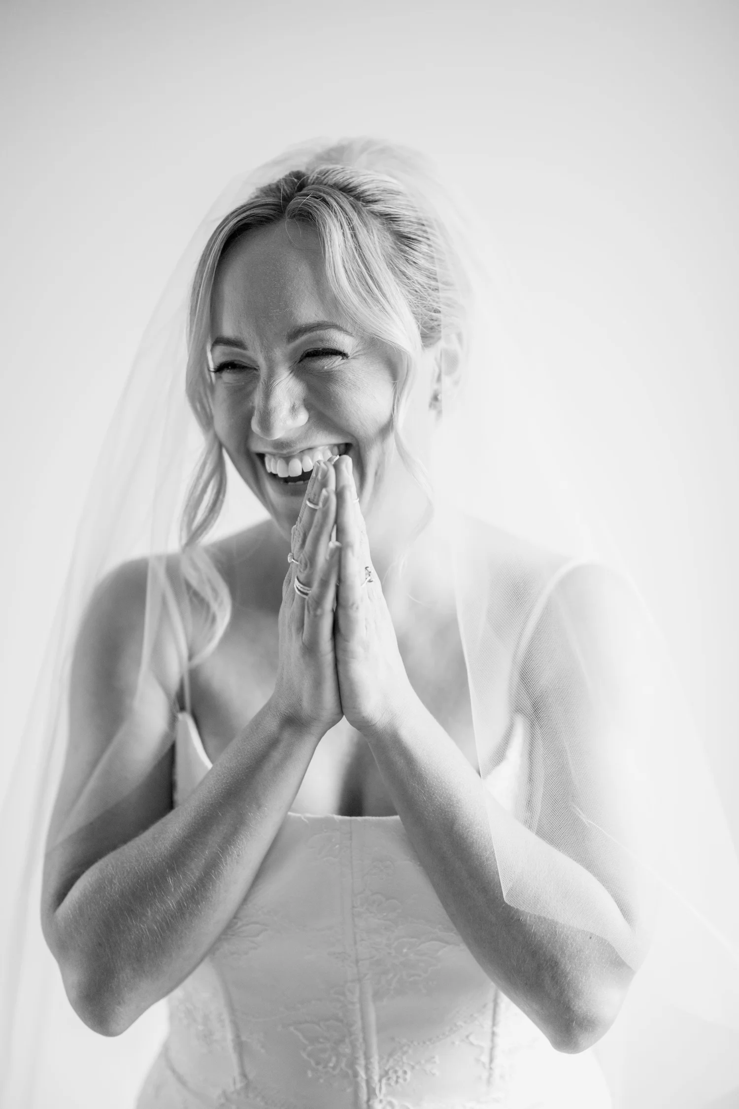 A bride beaming with her hands pressed together