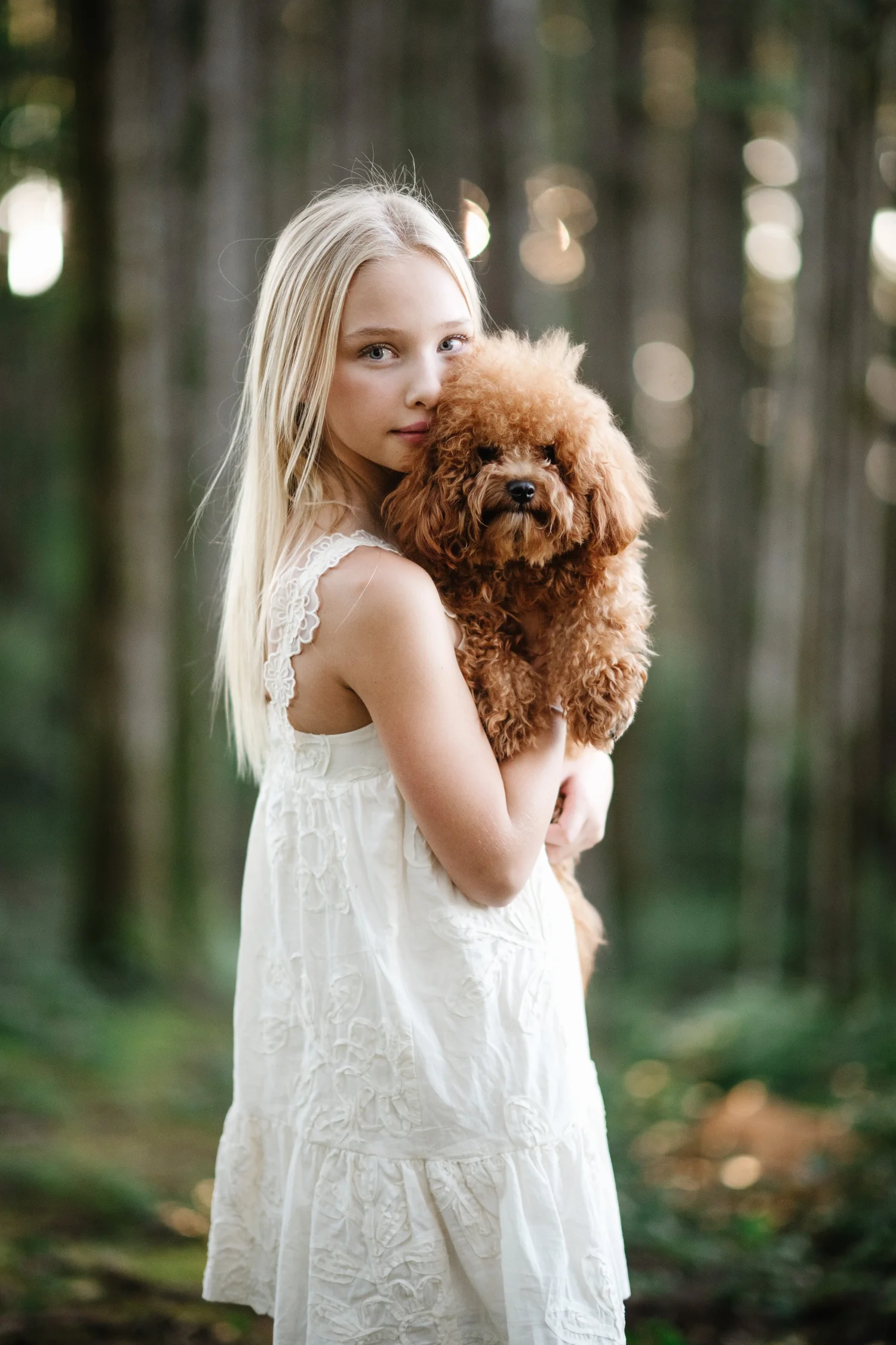 A girl in a white dress hugging her puppy in the forest