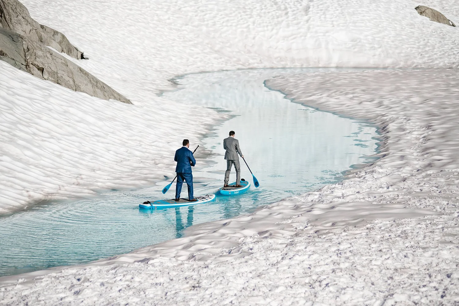 A couple paddleboarding on a turquoise glacier pool