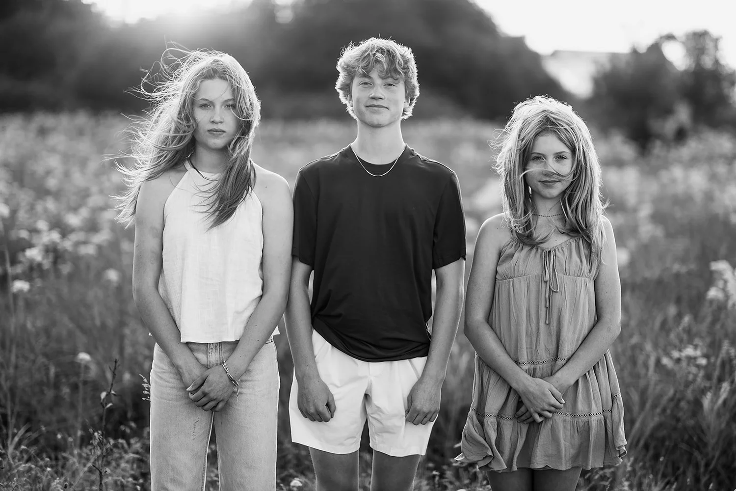 Three siblings standing together in a summer field, in black and white