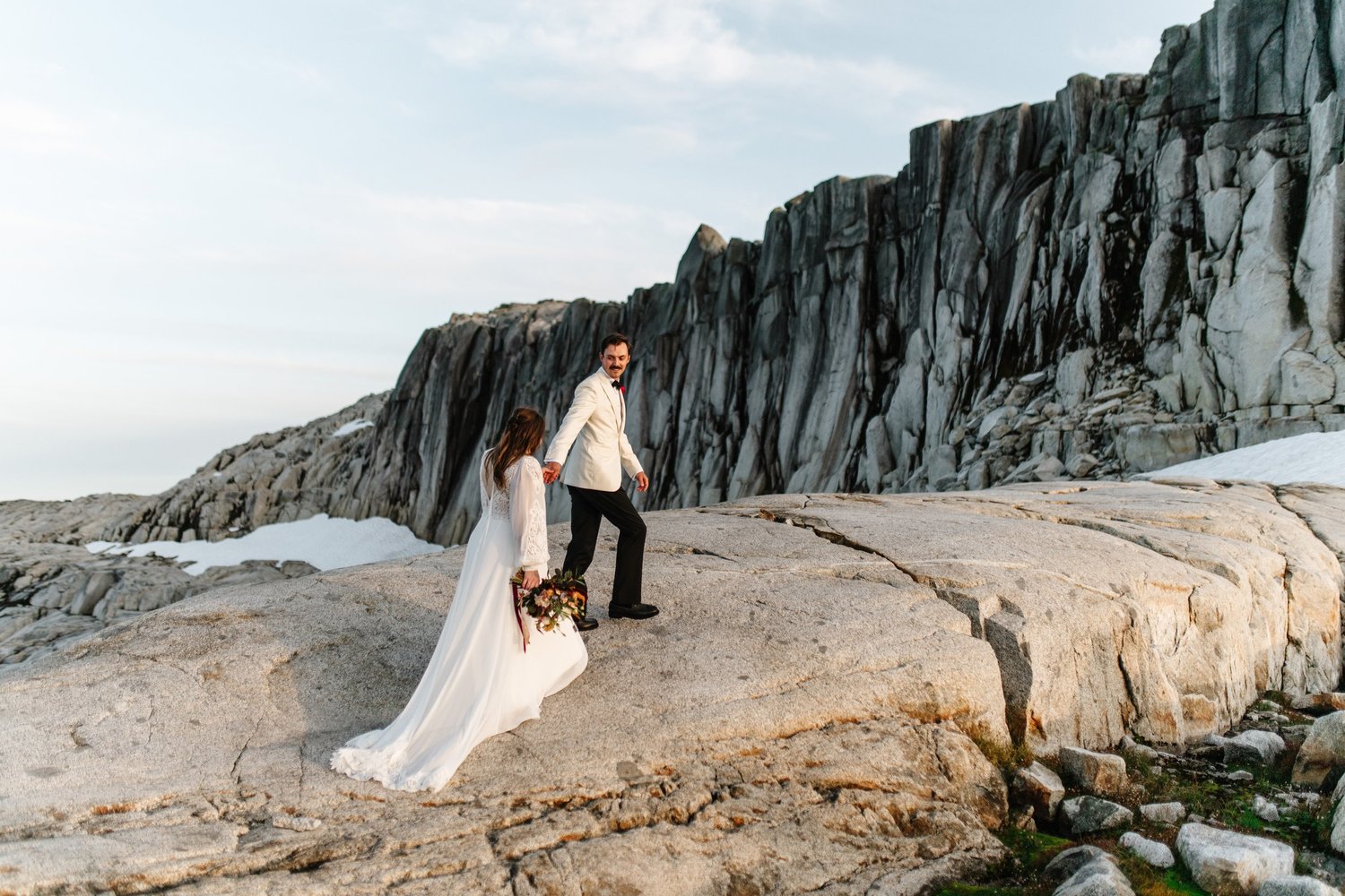 A couple beneath a dramatic rock wall in the alpine