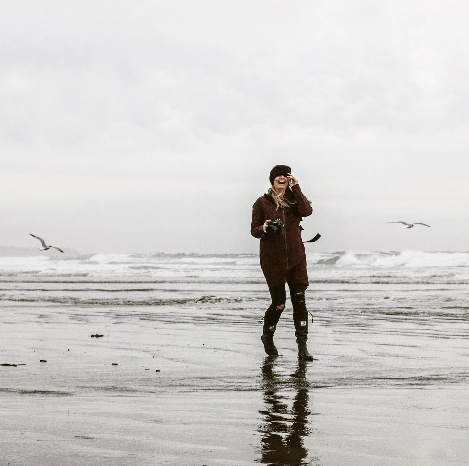 Photographer Erin Wallis laughing on a stormy beach with her camera