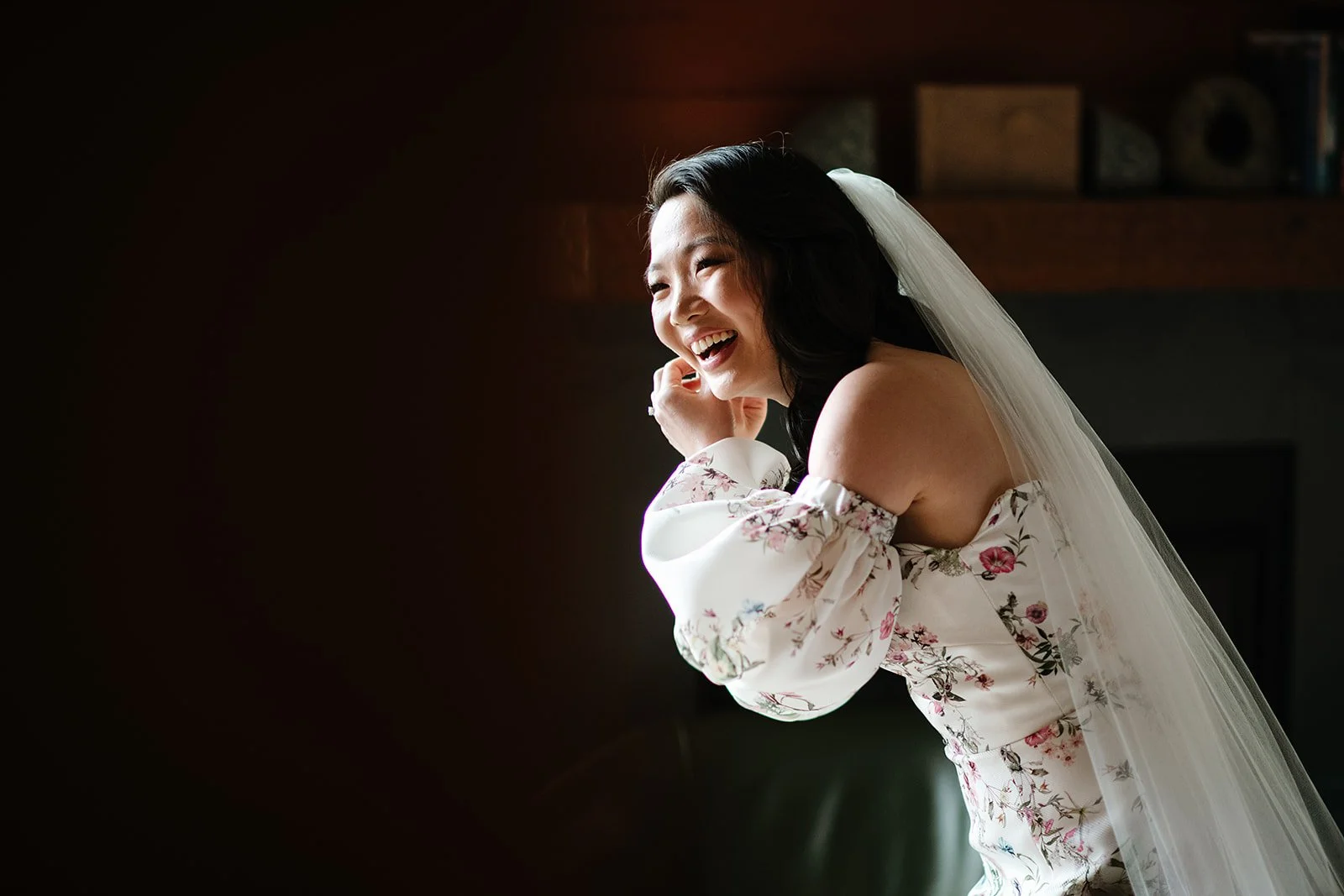 A bride laughing in warm window light on her wedding morning