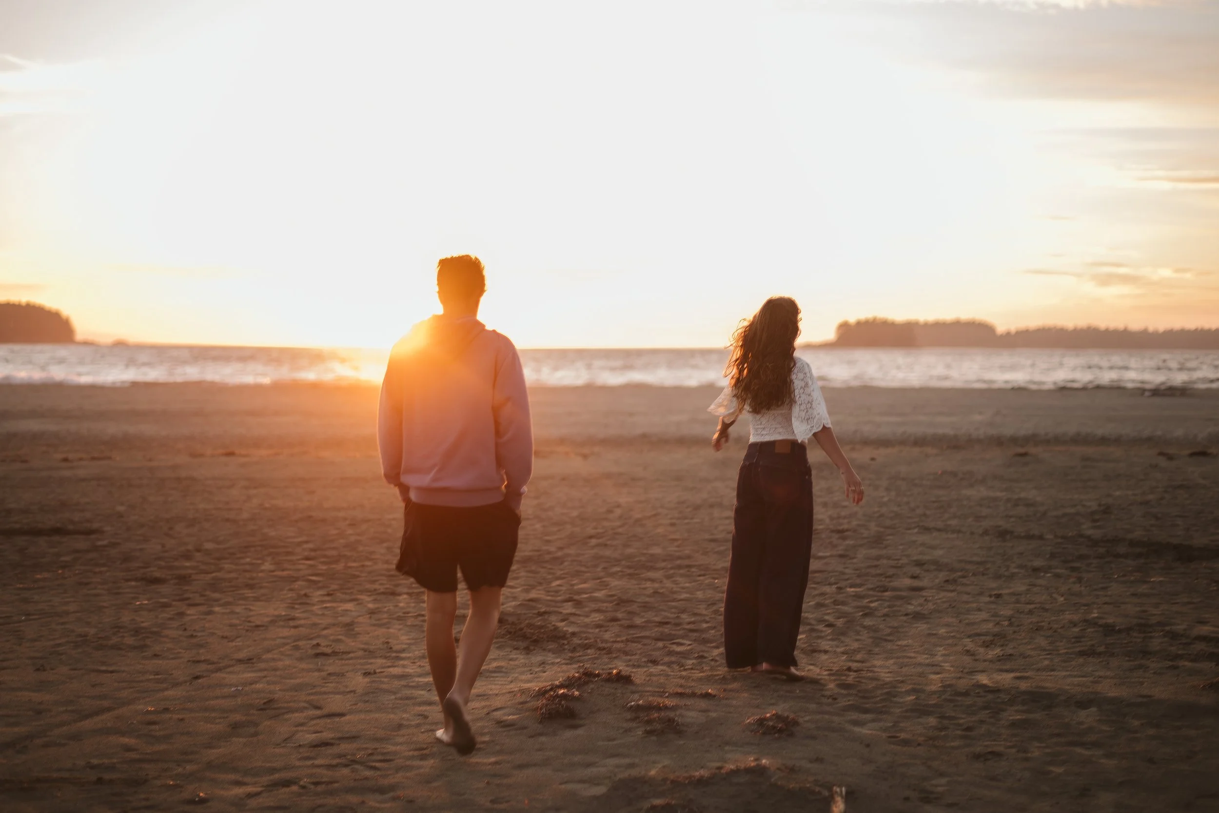 Two teenagers walking across a Tofino beach toward the setting sun