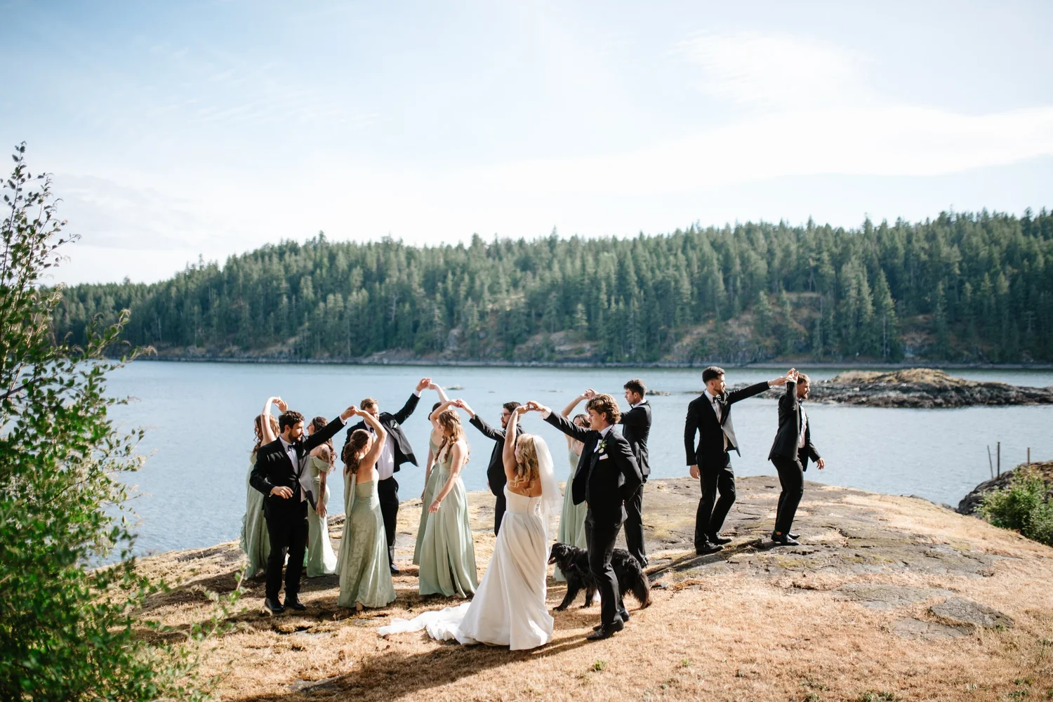 The wedding party cheering on the rocks by the water