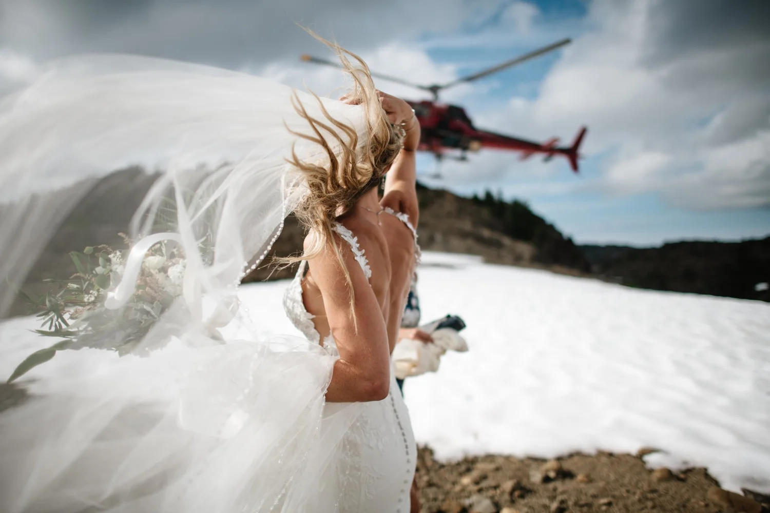A bride with windblown hair as a helicopter lands on the snow