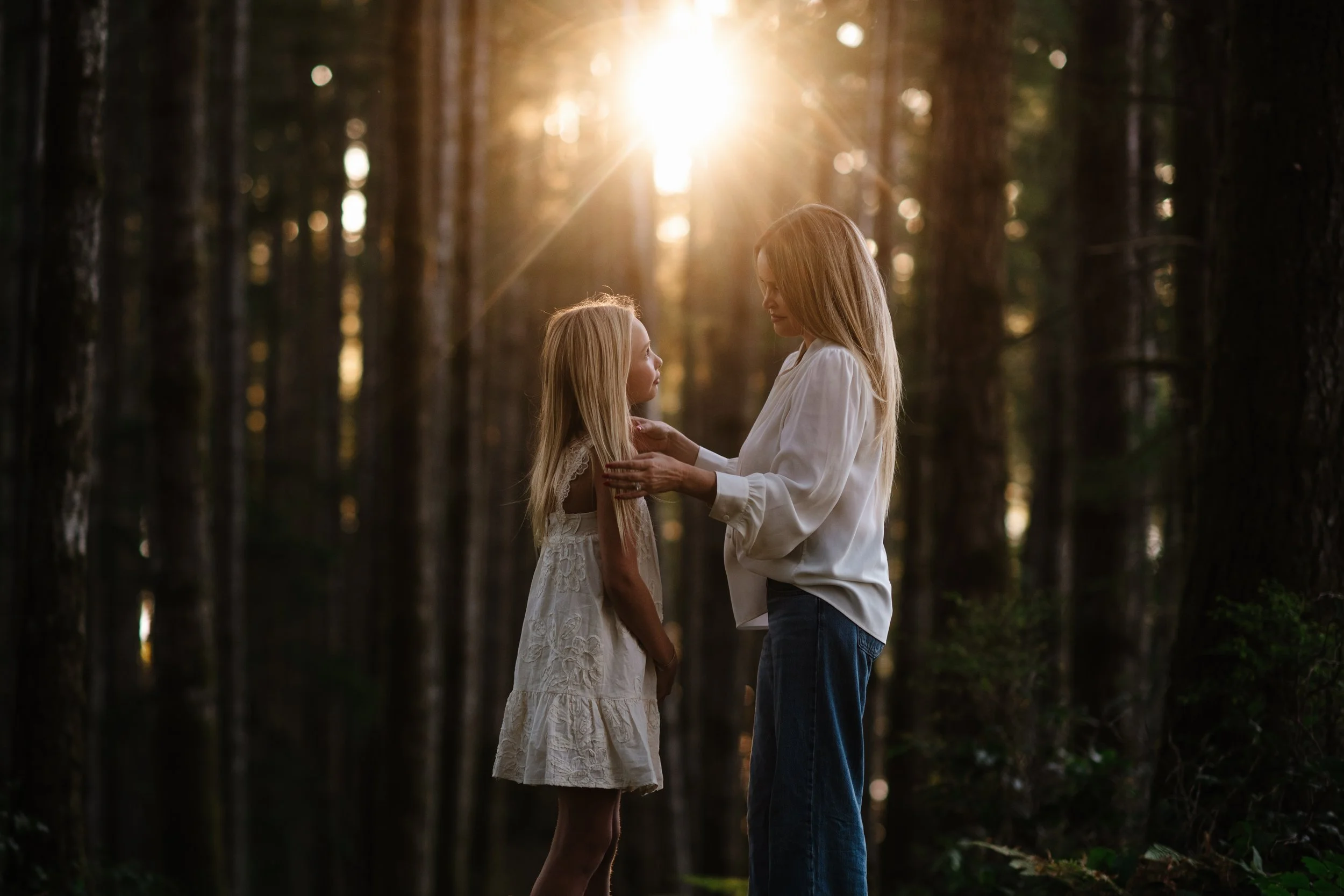 A mother and daughter facing each other in golden forest light on Vancouver Island