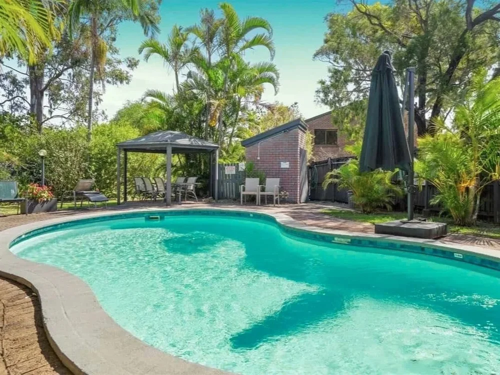 Outdoor pool with shaded seating and tropical landscaping in a townhouse complex in Labrador QLD.