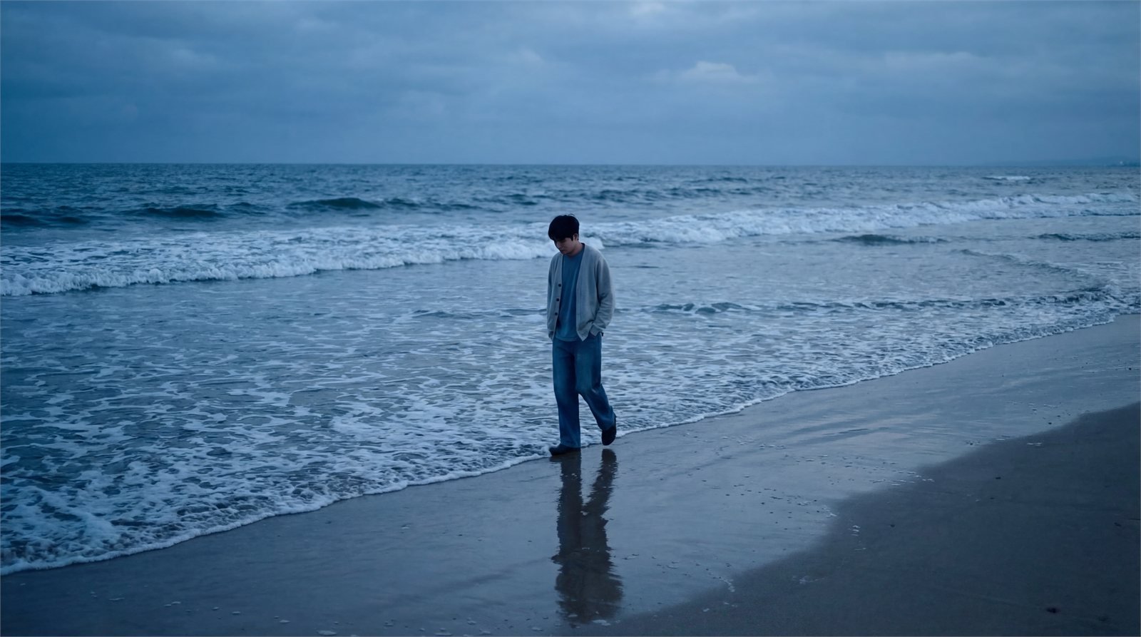 A lone figure walking the water line on an empty beach.