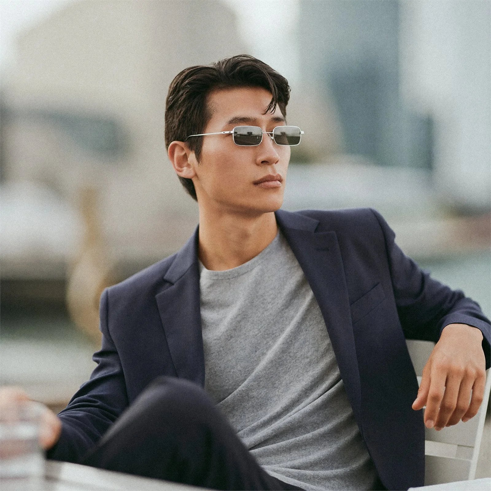 A man in a navy jacket and silver sunglasses, seated and looking away past the frame.