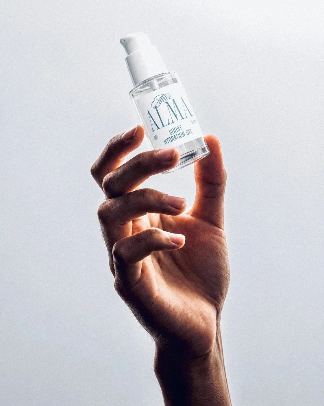 A hand holding the After Alma serum bottle against a pale sky.