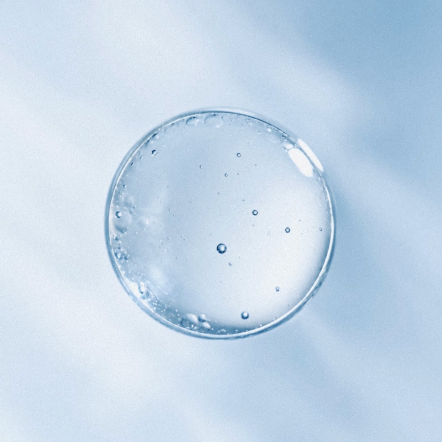 A single drop of oil suspended on pale blue.