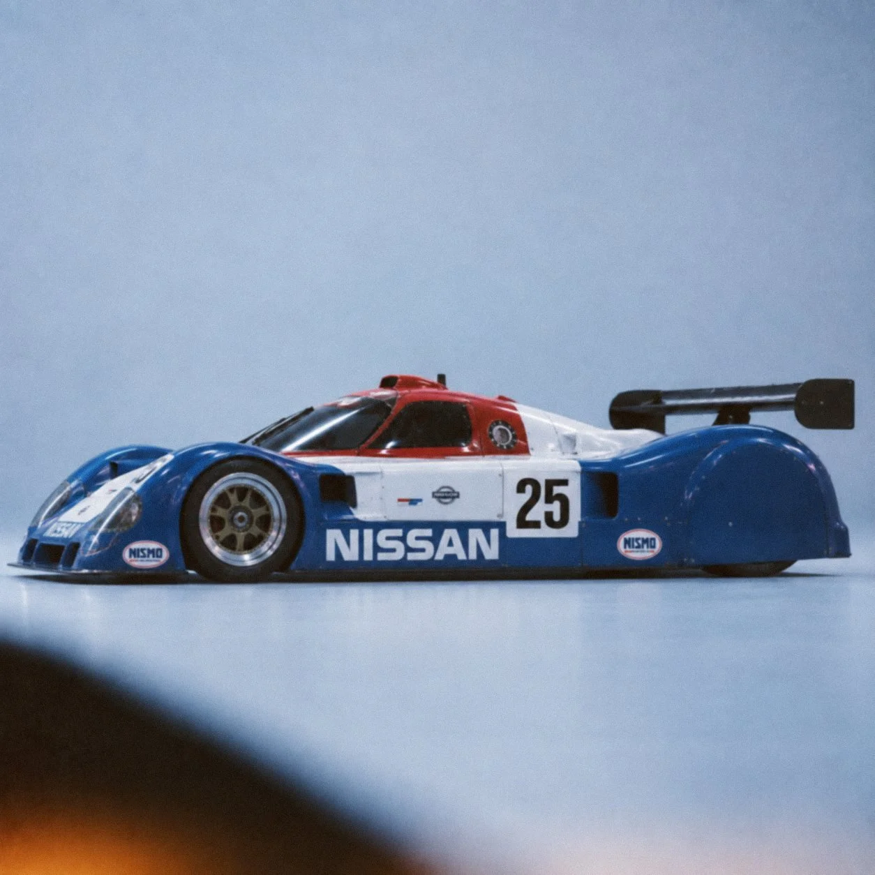 A side profile of the Nissan R89C, blue and white with the number 25.