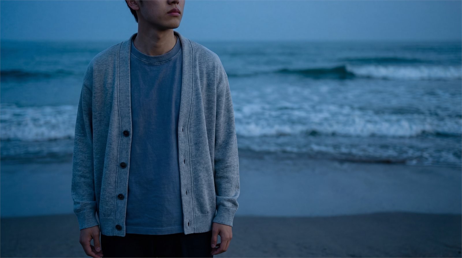 A figure standing on wet sand as a wave breaks behind them.