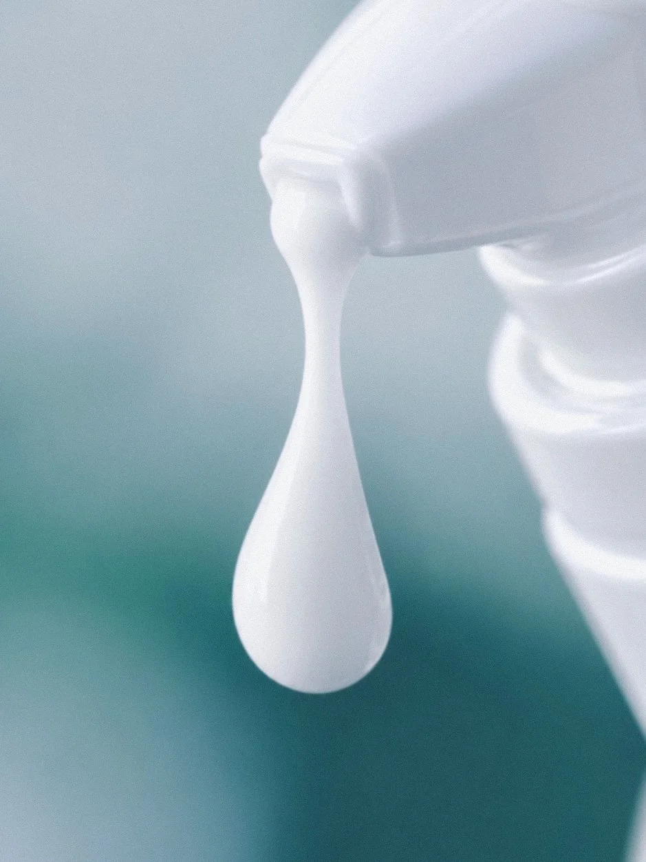 A white pump head dispensing a single drop onto a teal surface.