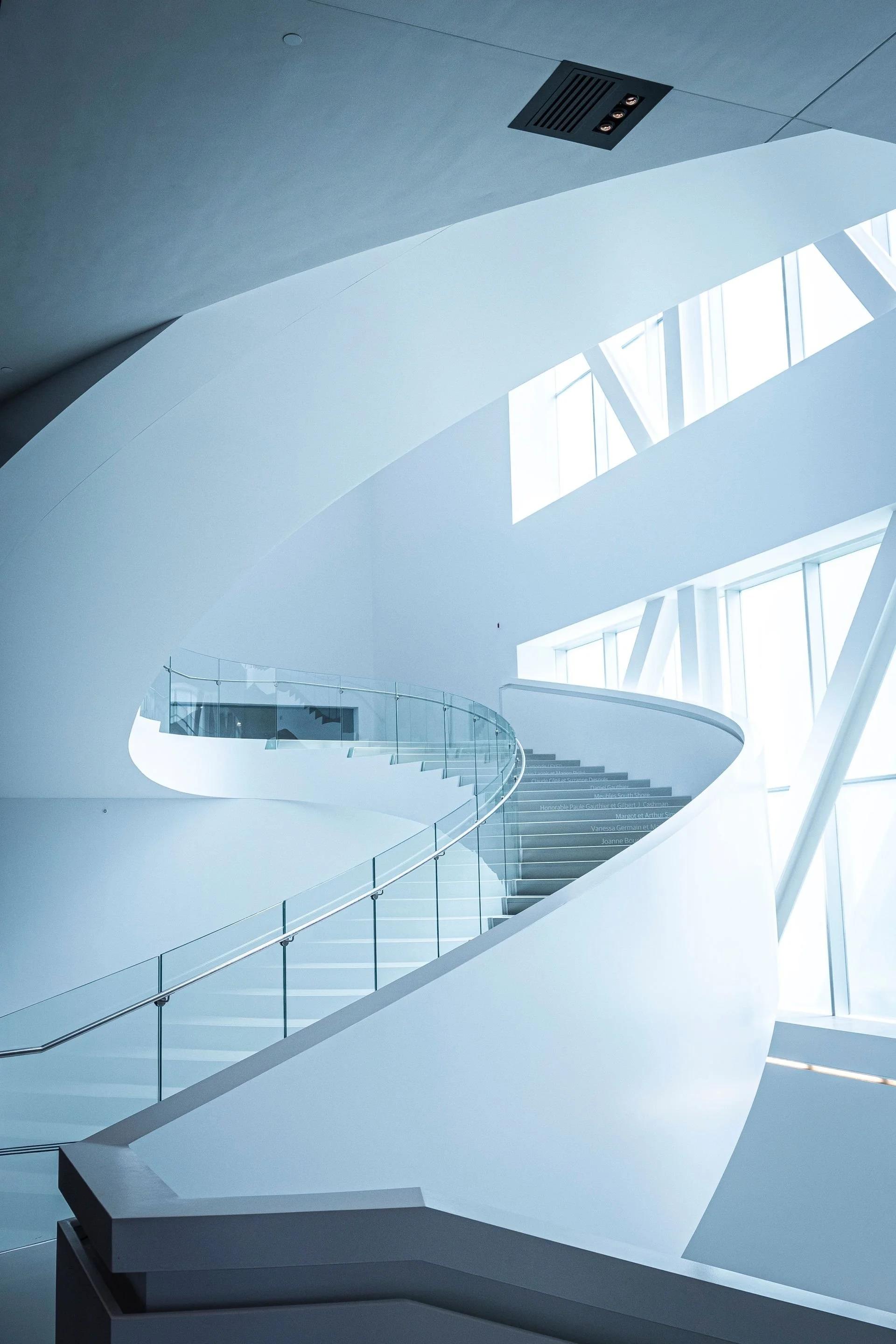 Sculptural white staircase with glass railing and tall windows
