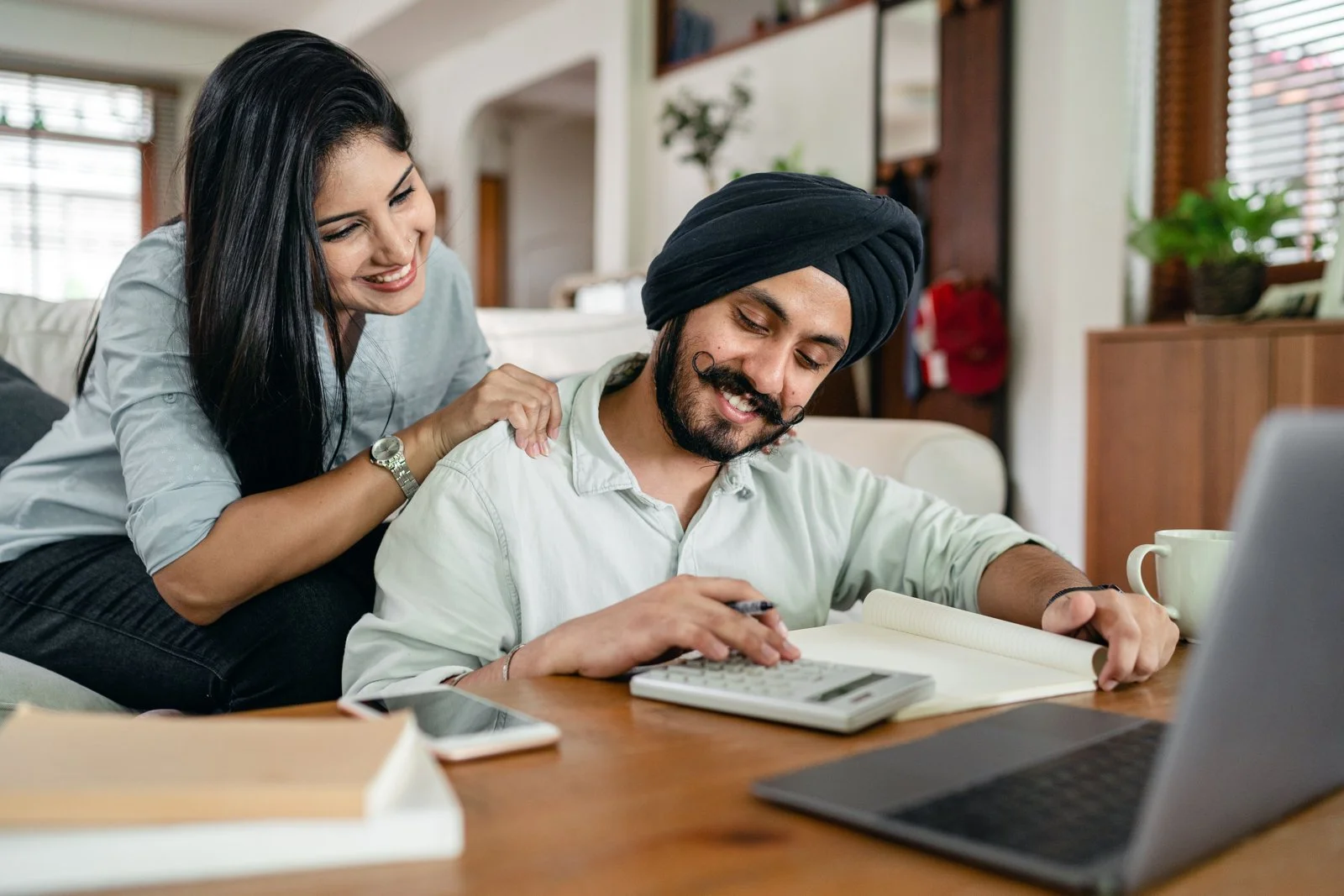 A smiling couple reviewing financial paperwork with a laptop and calculator
