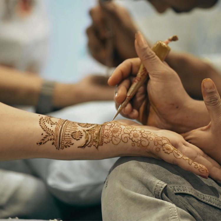 A hand applying a henna design to an arm