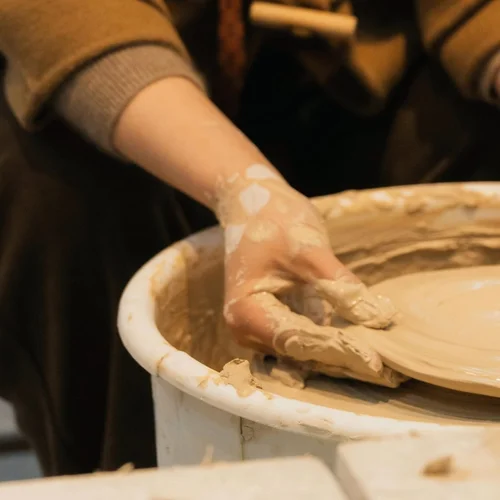 A clay-covered hand shaping a plate on a pottery wheel