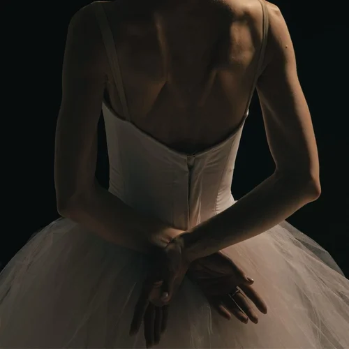 A dancer in a tutu with hands clasped behind her back