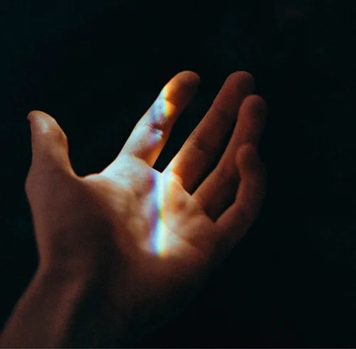 A hand lit by a band of rainbow light against black