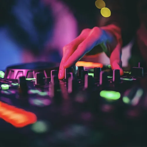 A hand turning knobs on a DJ mixer in colored light