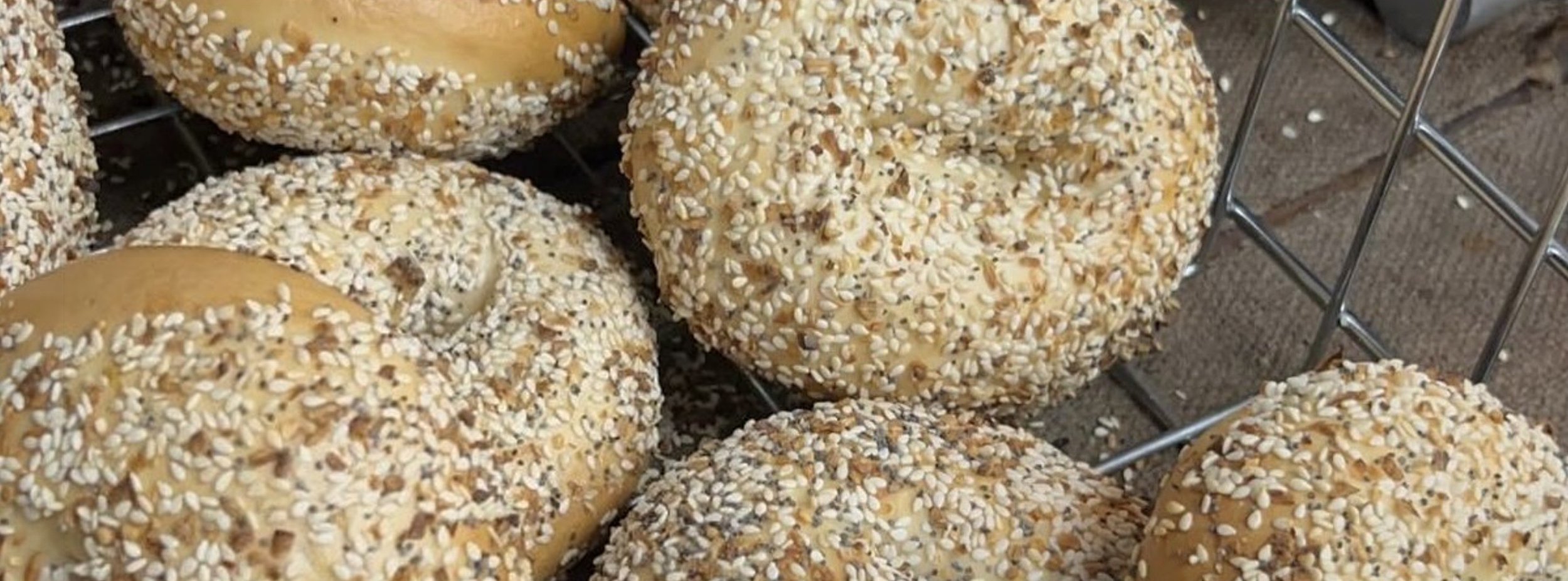 Fresh sesame and everything bagels cooling on a wire rack at Bagel Bob in Houston