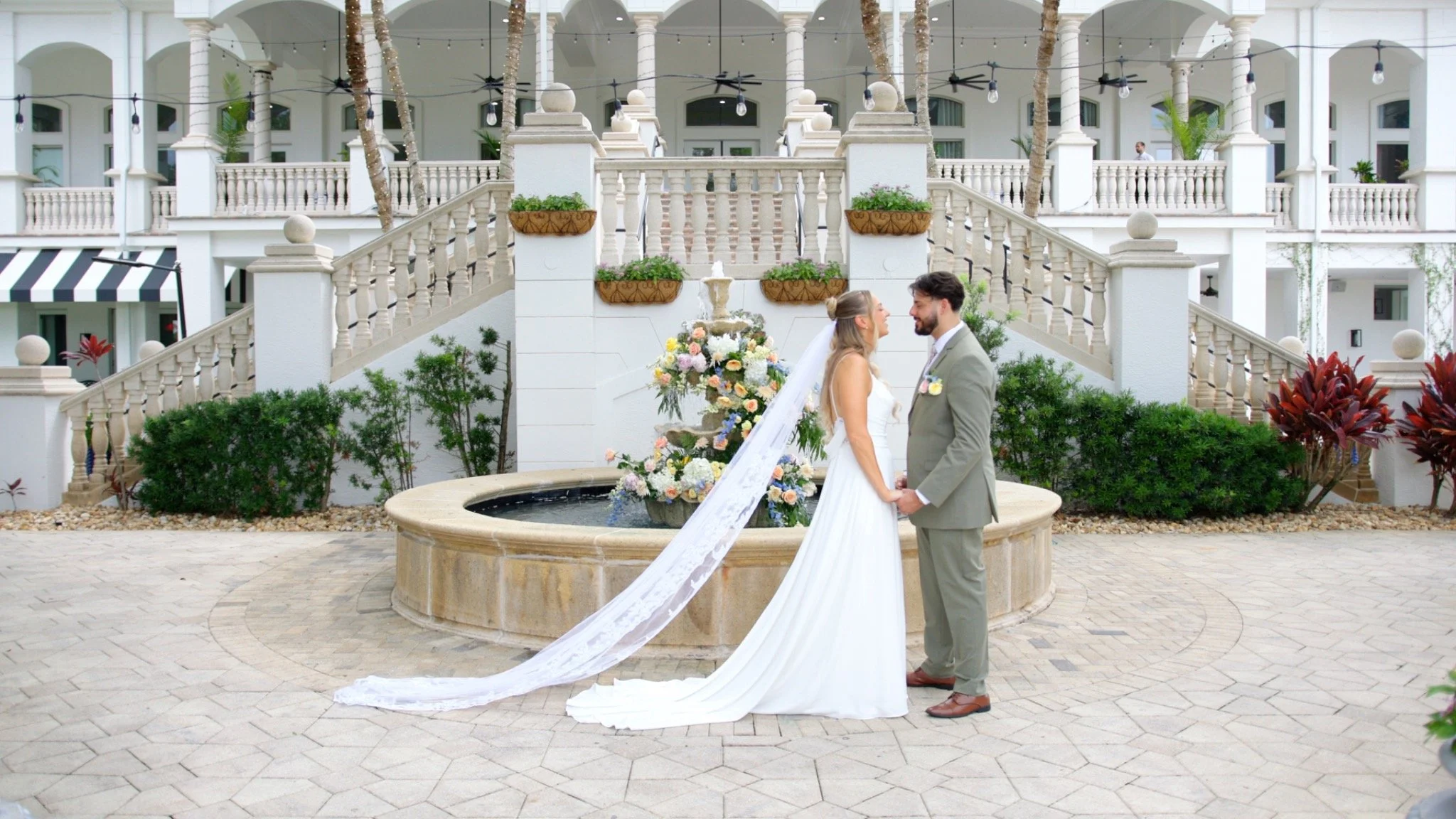 Bride and groom holding hands beside a flower-filled fountain