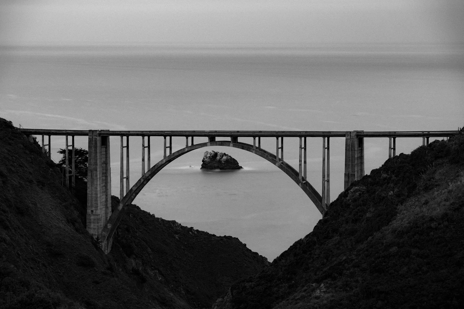 An arched concrete bridge spanning a coastal canyon, in black and white