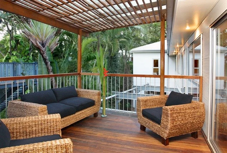 Upper deck under a timber pergola, with cane lounge chairs and treetop views
