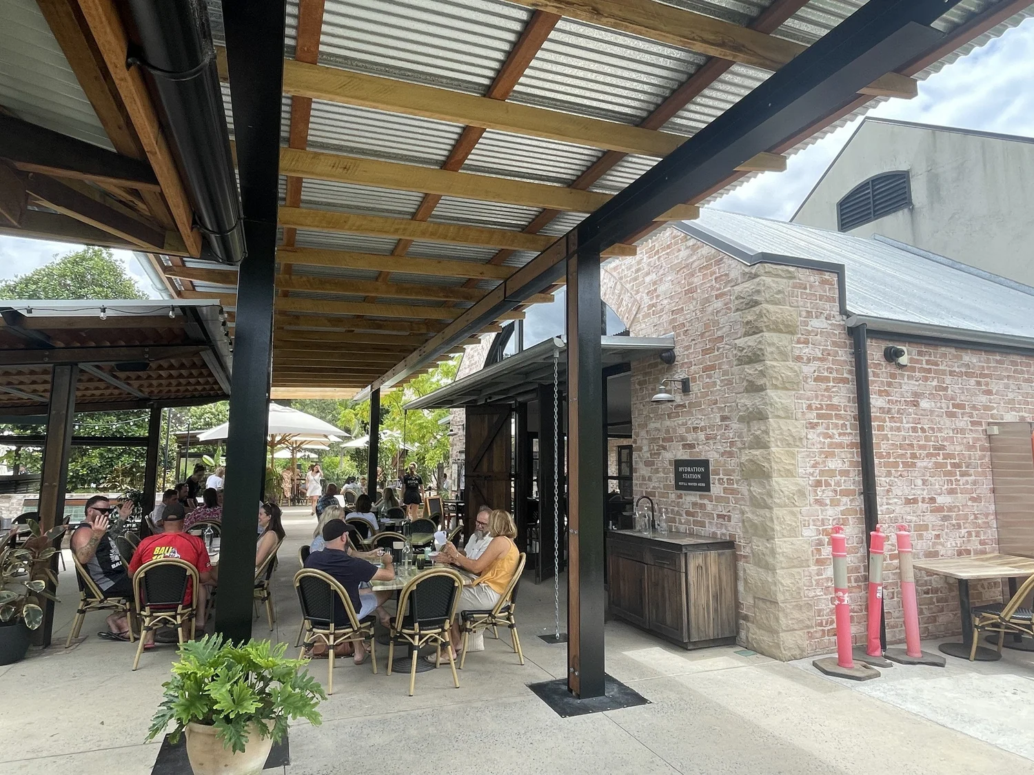 Visitors at tables under a timber-framed verandah roof beside the brick cellar door building