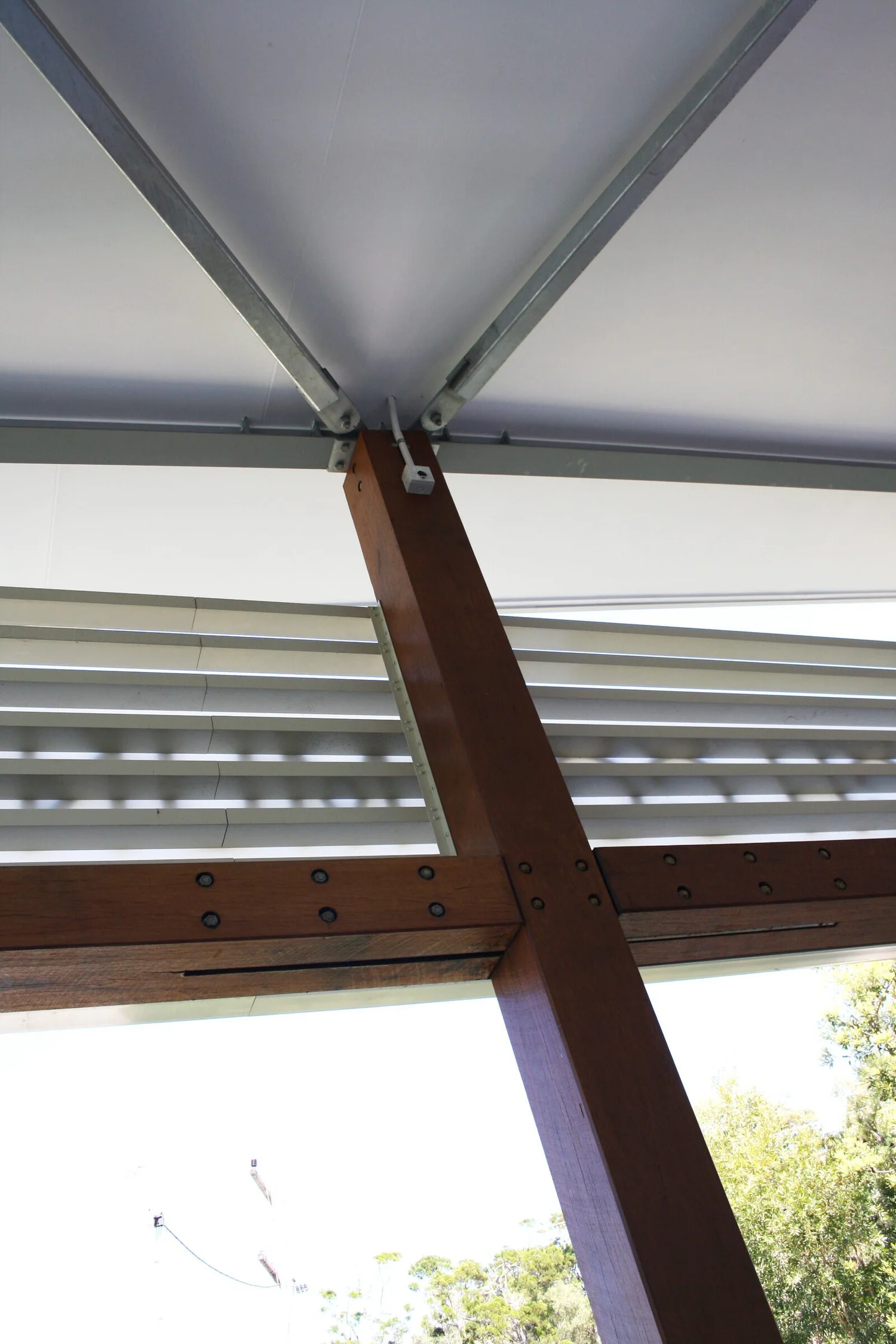 A laminated timber post meets the steel verandah frame under the louvres