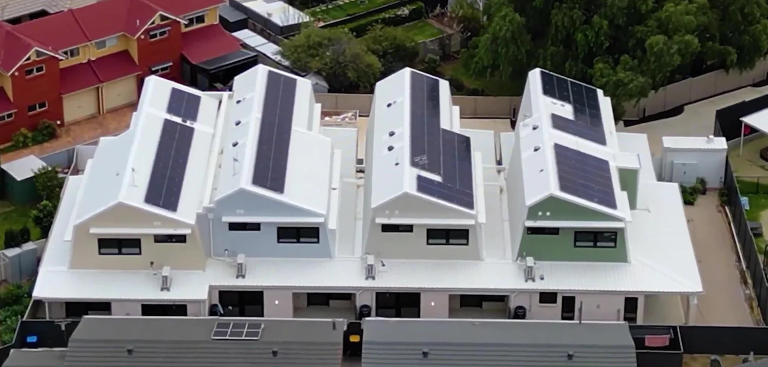 The four townhouses from the rear: folded roofs, each with its own solar panels, above the ground-floor terraces