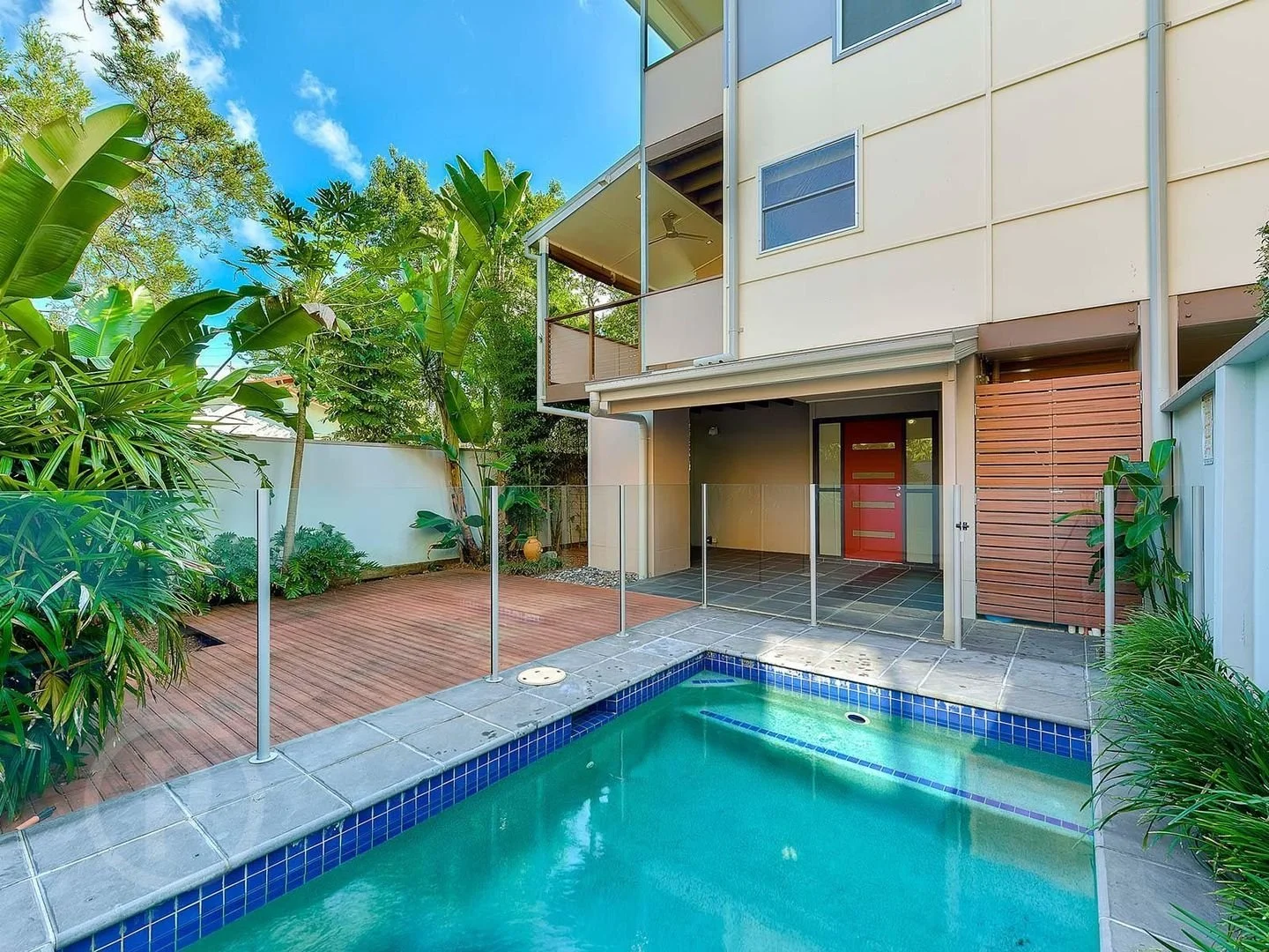 A pool terrace below a white facade with balconies and a timber screen