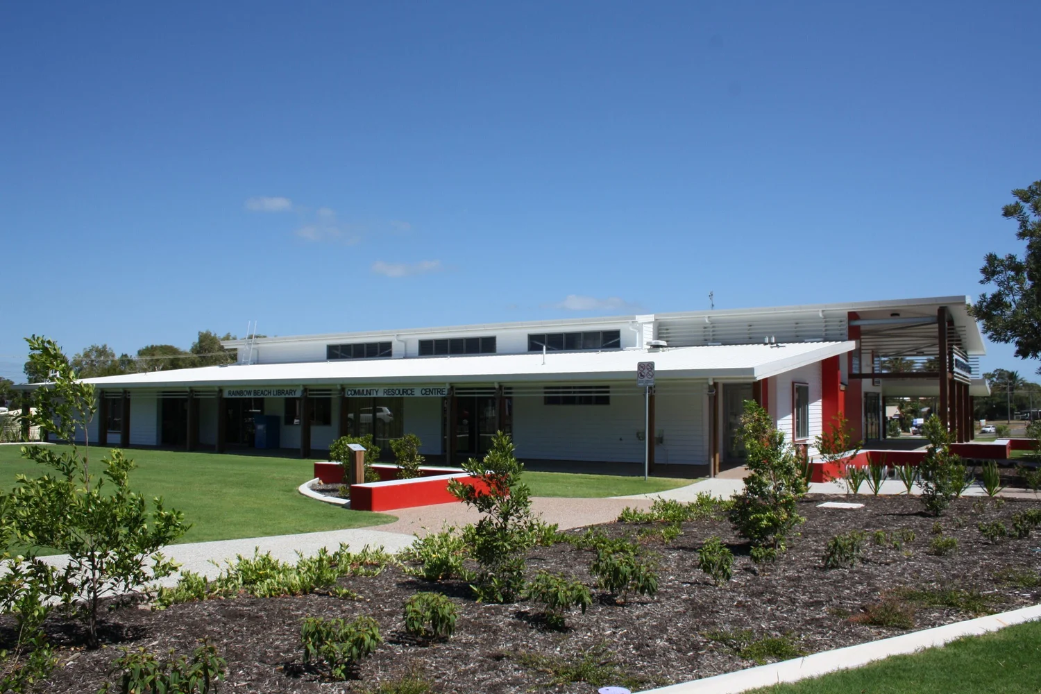 The hall across new native gardens, with the red blade wall at the entry