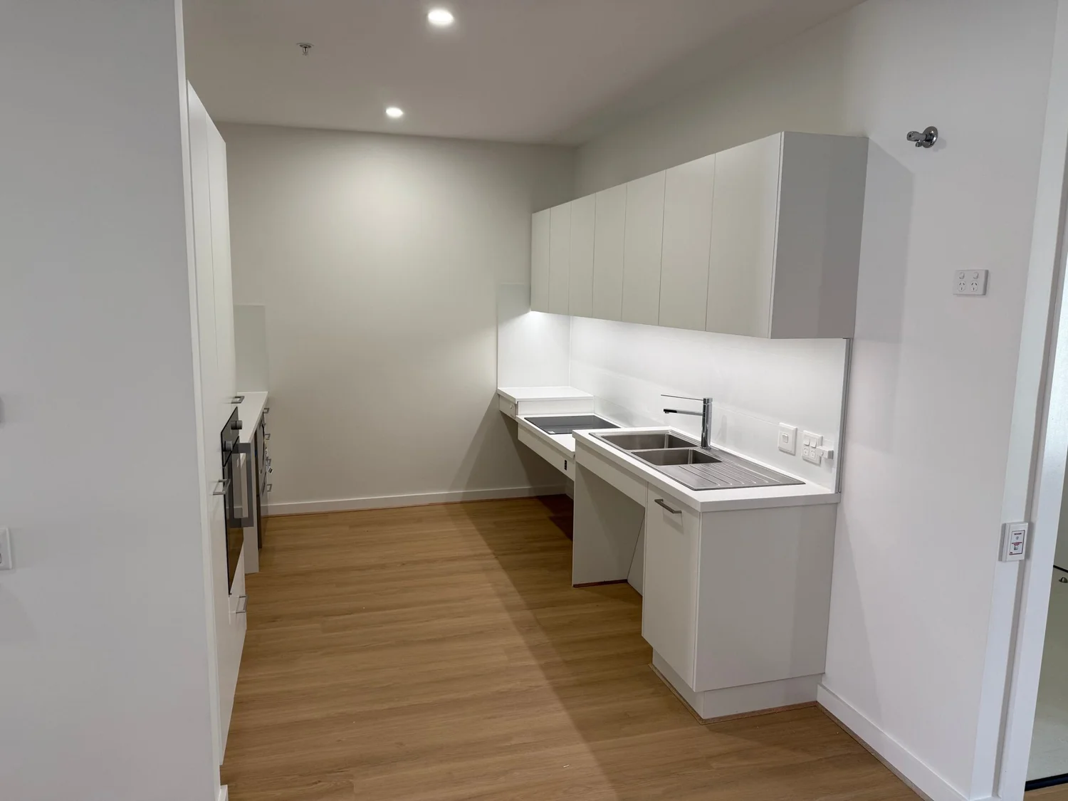 Galley kitchen with a wall oven opposite, and sink and cooktop benches with open knee space beneath for a wheelchair