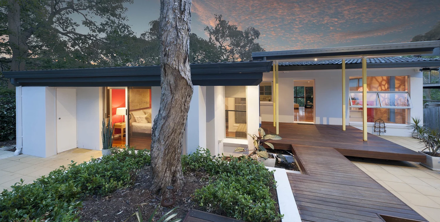 The house at dusk among gum trees, with a timber deck stepping down to the garden