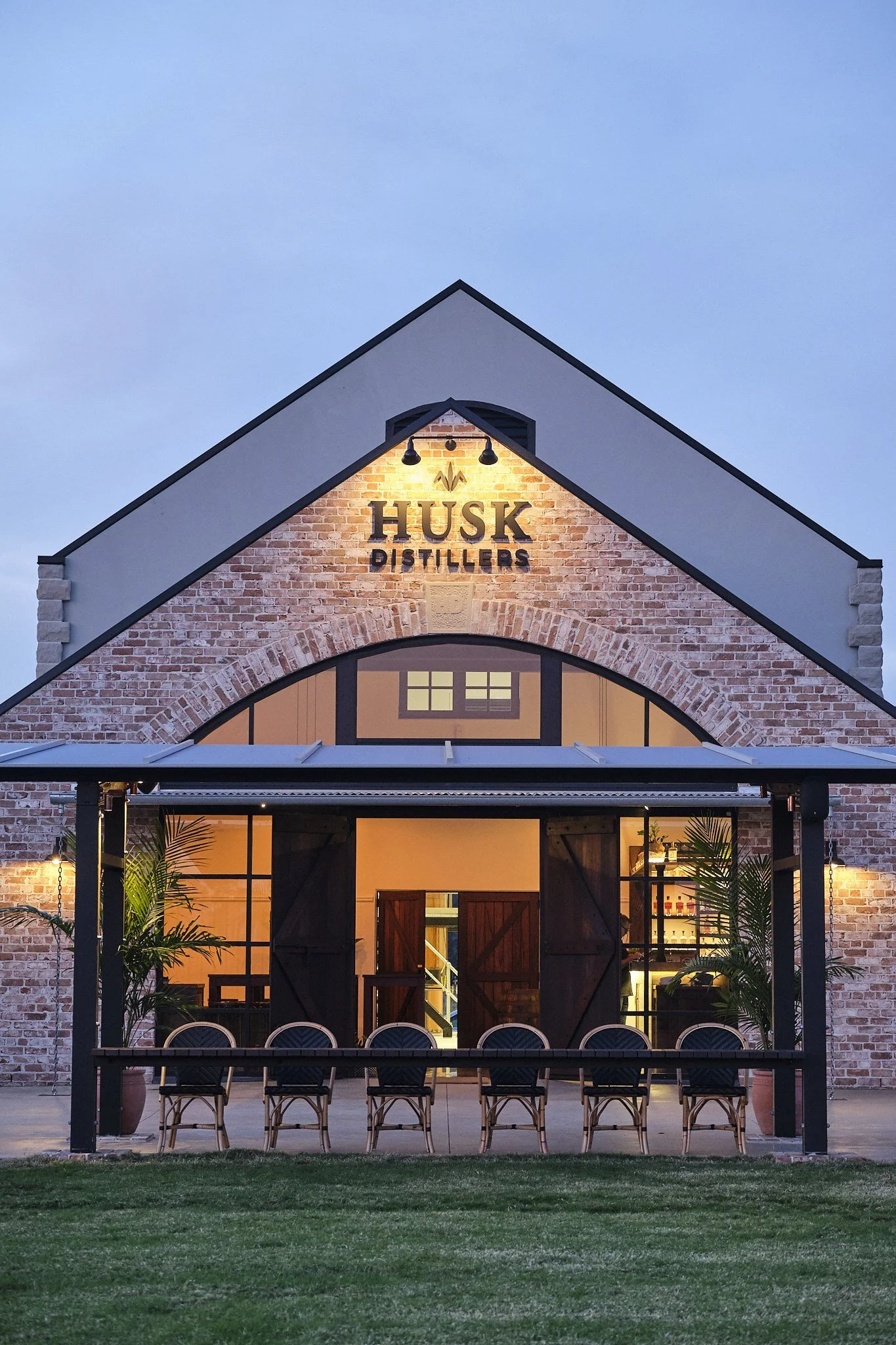 The brick gable with the Husk Distillers sign above an arched window and a verandah set with tables
