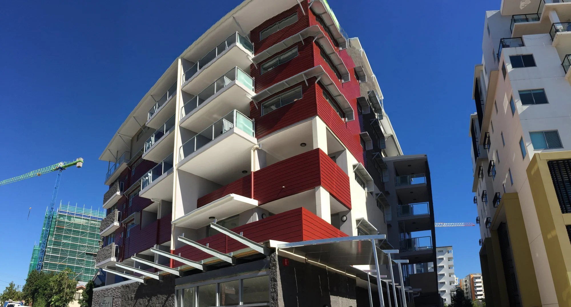 The completed building from the street, with red cladding, stone-clad balconies and a glass entry awning