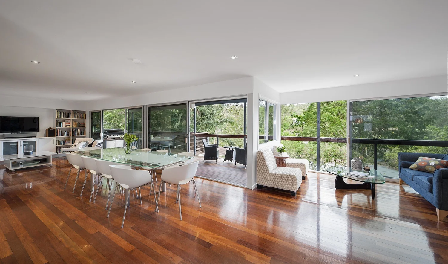 Long living and dining room with timber floors and full-height glazing to the trees
