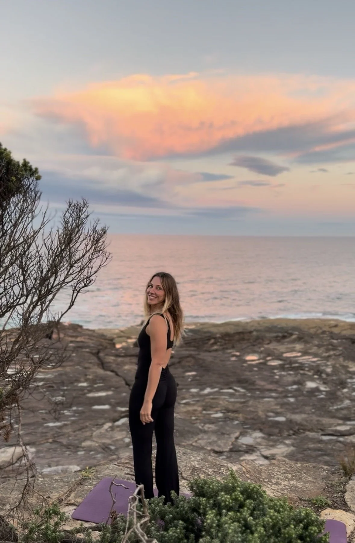 Francesca smiling beside the ocean beneath a pink sunset