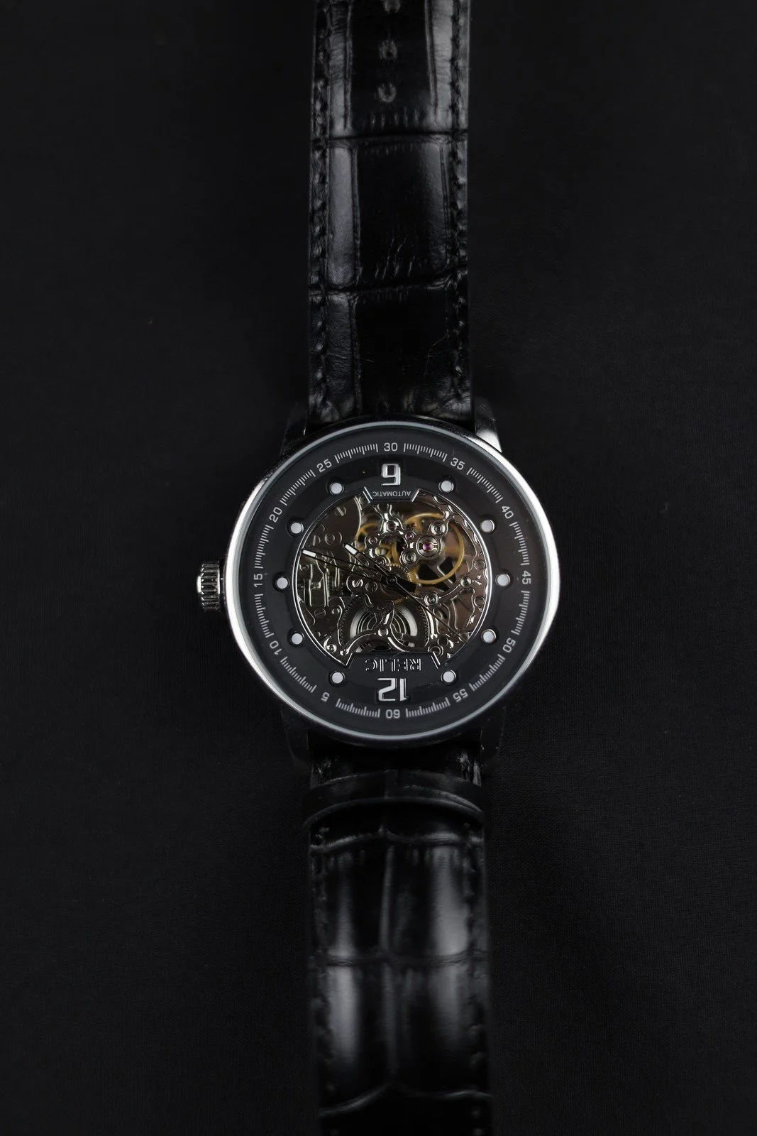A wristwatch with visible mechanical details and a black strap against a dark background.